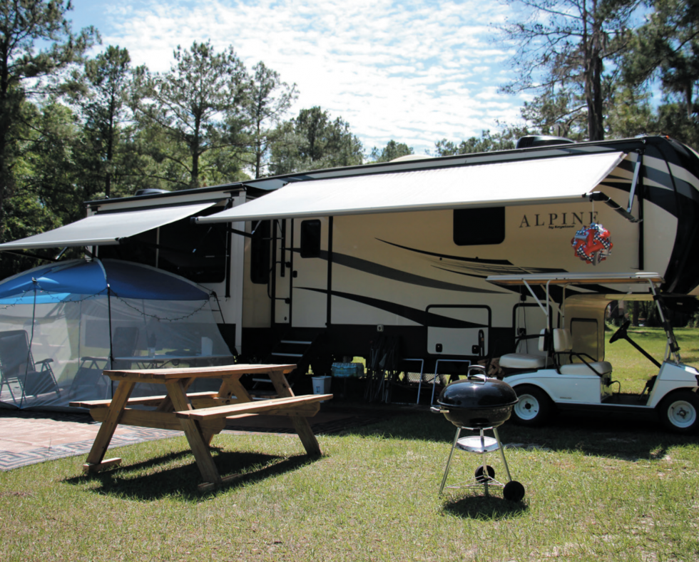 A camper, picnic table, grill, and golf cart sit in a vast green campground at the Spirit of Suwannee Music Park.